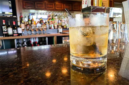 Image: mixed drink sitting on a bar with liquor bottles in background